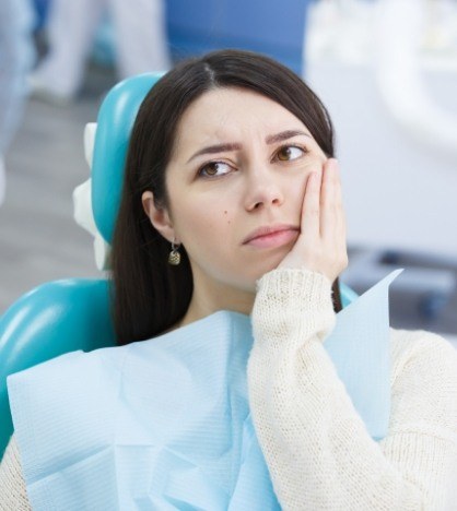 Woman in dental chair touching her cheek in pain