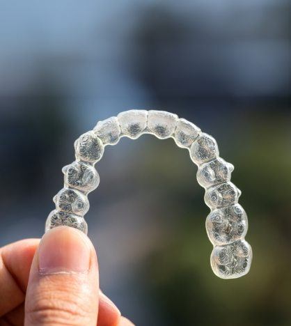 Hand holding an Invisalign clear aligner in New York