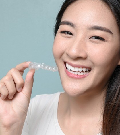 Young woman grinning while holding an Invisalign aligner