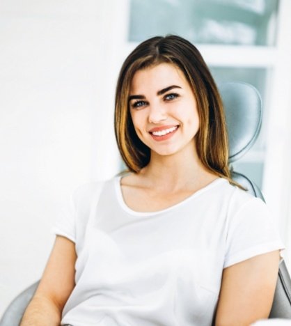 Young woman smiling in dental chair after restorative dentistry in New York