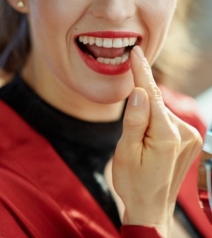 Woman with red lipstick looking at her teeth in mirror