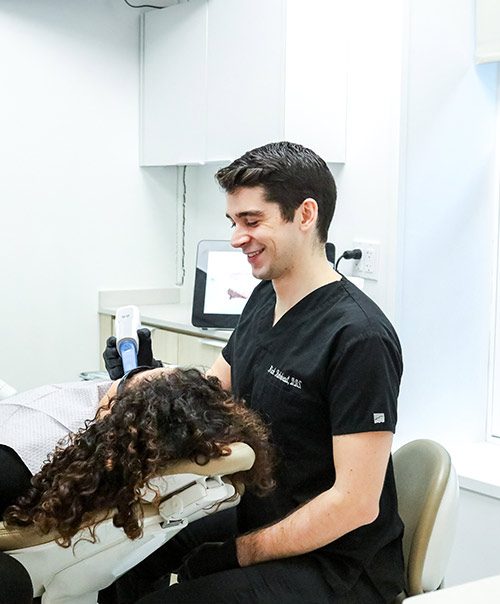 Smiling dentist in black scrubs treating a patient in a New York dental crowns exam chair