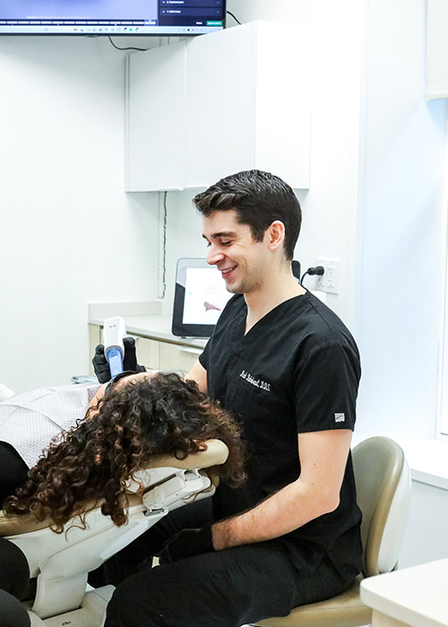 Smiling dentist in black scrubs treating a patient in a New York dental crowns exam chair