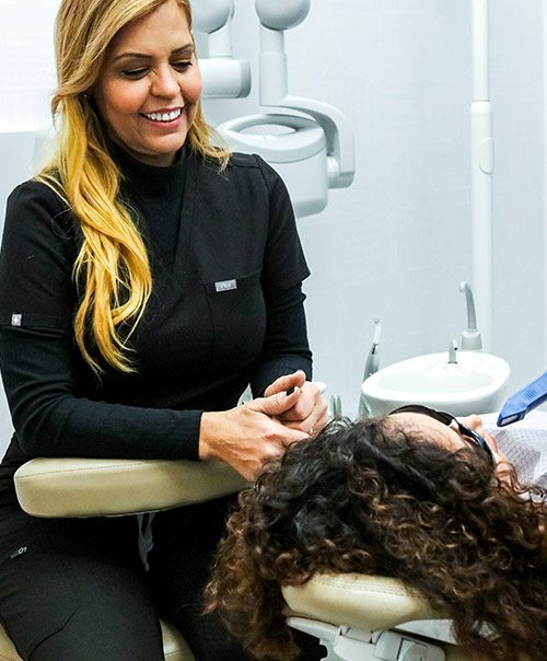 Smiling hygienist in black scrubs holding a patient's hand before teeth cleaning in New York