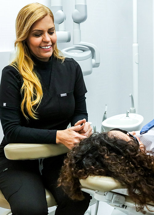 Smiling hygienist in black scrubs holding a patient's hand before teeth cleaning in New York